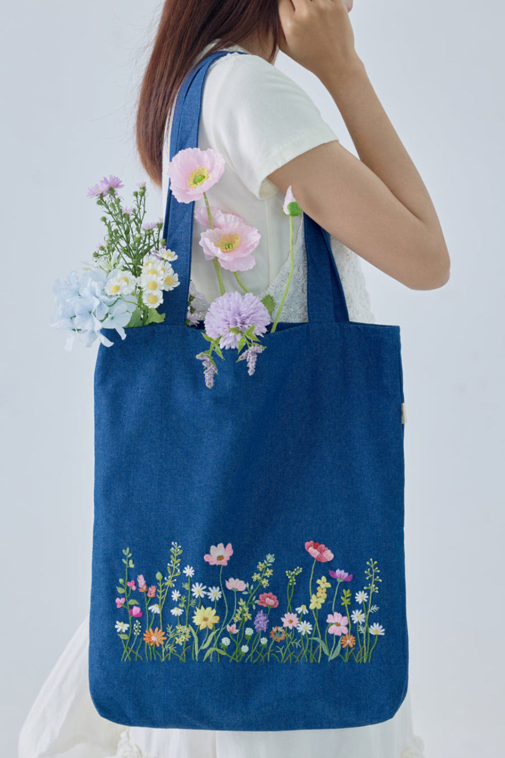 Blush Garden Hand Embroidery Jean Tote Bag featuring colorful floral embroidery on dark blue denim, styled with pastel flowers for a soft, feminine look.