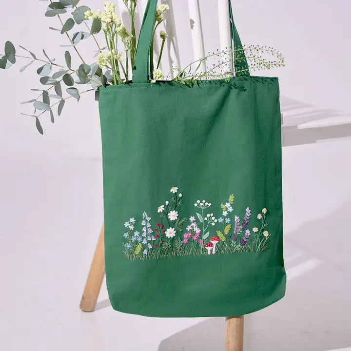 Green Wildflowers Garden Embroidery Tote Bag with floral design and mushroom detail, displayed on a chair with greenery inside.
