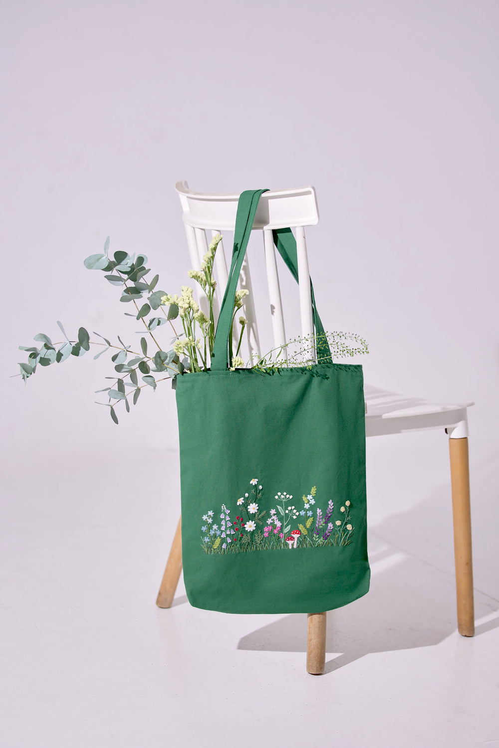 Wildflowers Garden Embroidery Tote Bag in green color shown hanging on a white chair, featuring colorful floral embroidery.