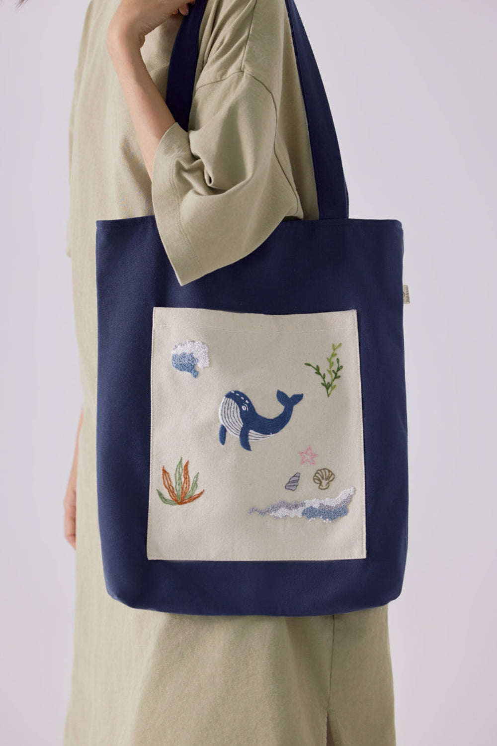 Blue Whale Embroidery Tote Bag Navy featuring ocean-themed embroidery with a whale, coral, and seashell on a front pocket, ideal for casual outfits.