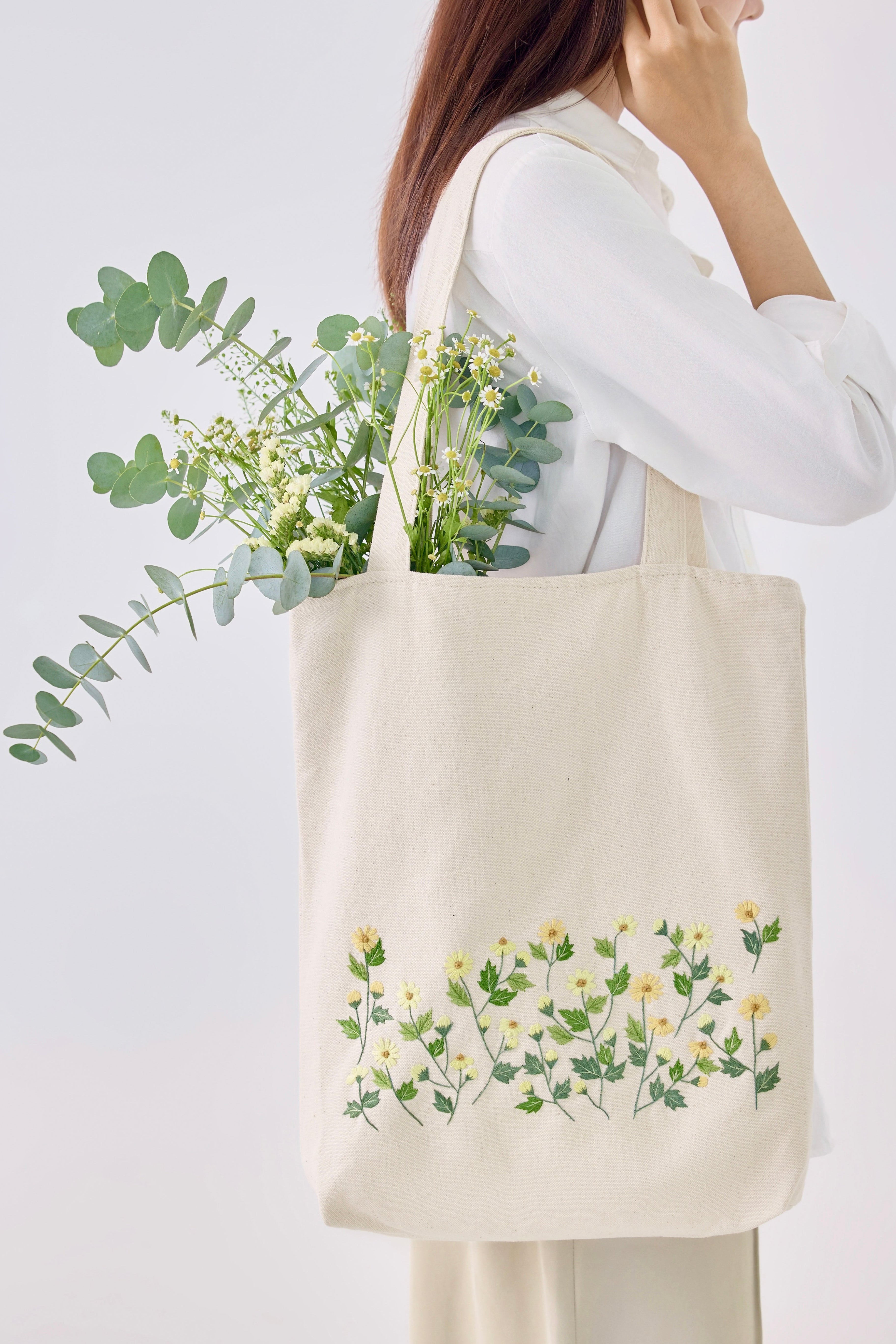 Yellow Daisy Embroidery Tote Bag with floral design carried on shoulder, styled with white blouse and beige pants for casual look.