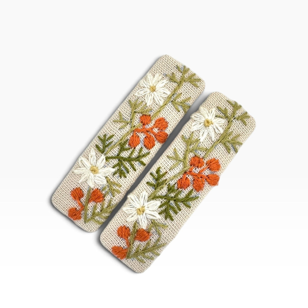 Two rectangular woven hair clips with embroidered white daisies, orange flowers, and green leaves on a cream background, shown on a plain white background.