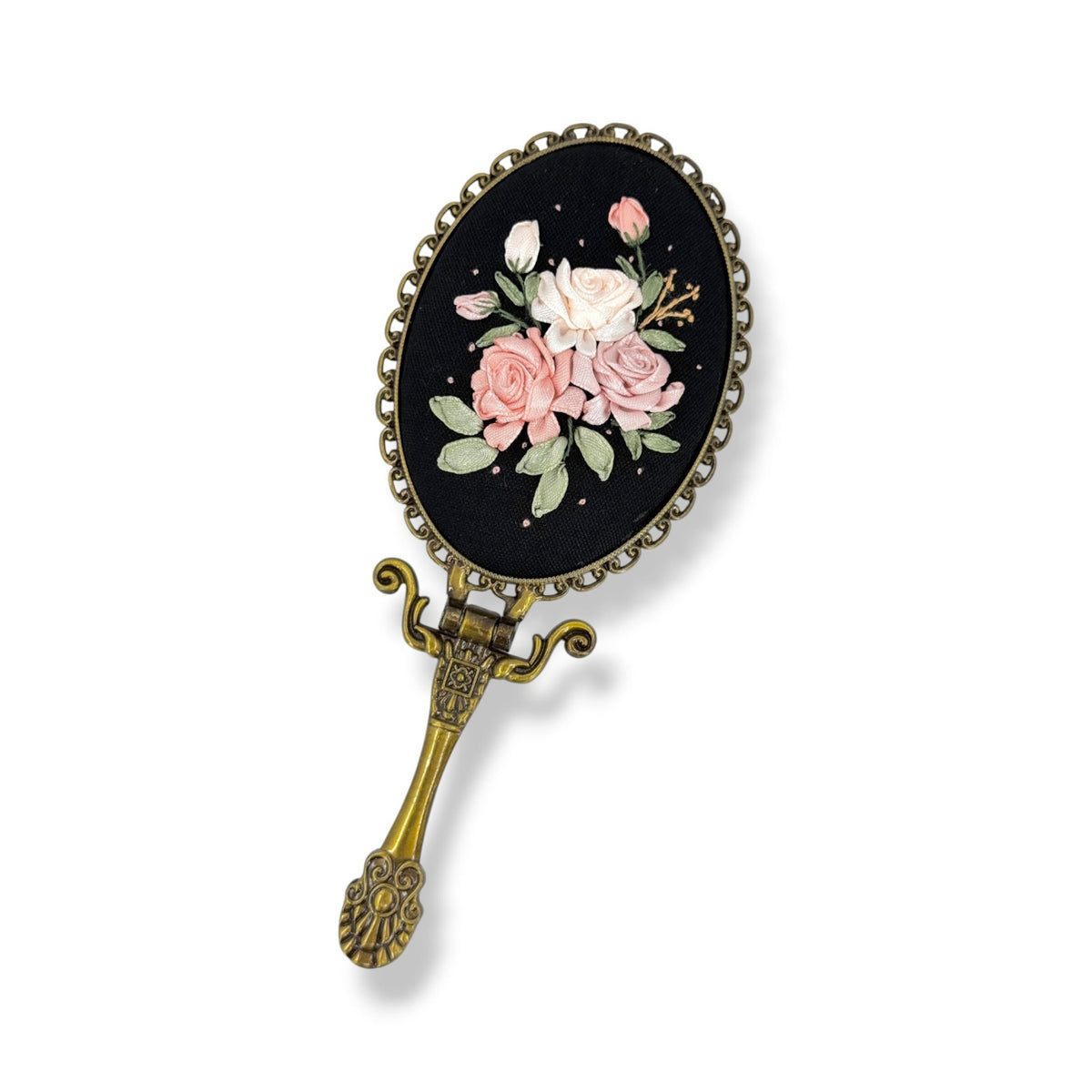 An antique-style oval hand mirror with a black enamel face featuring pink and white roses, green leaves, and a decorative gold-toned metal frame and handle.
