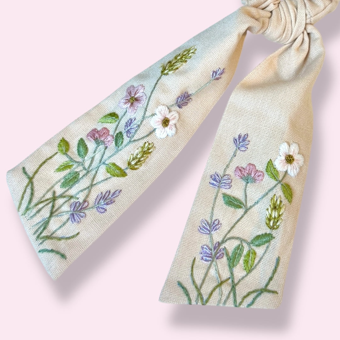 Close-up of hand-embroidered floral design on cream scrunchie scarf, ideal cute hair accessory for women and teenage girls.