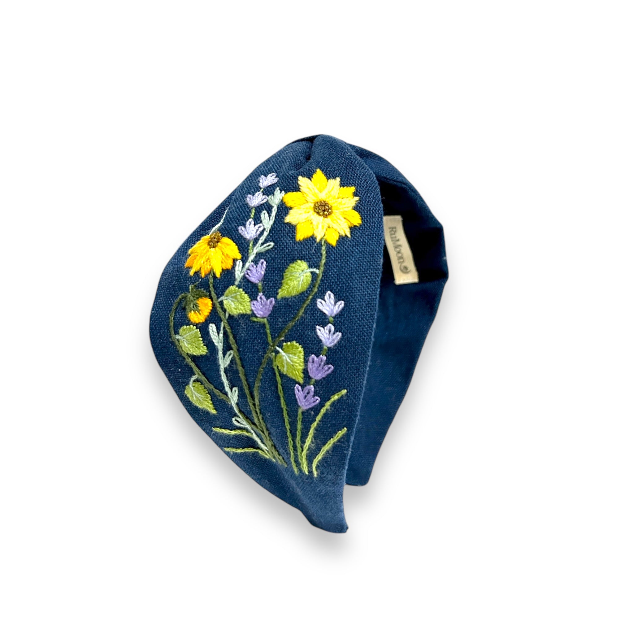 Emerald Field Blossom Embroidered Linen Headband by Rumoon Handmade featuring yellow and purple floral embroidery on dark blue fabric.