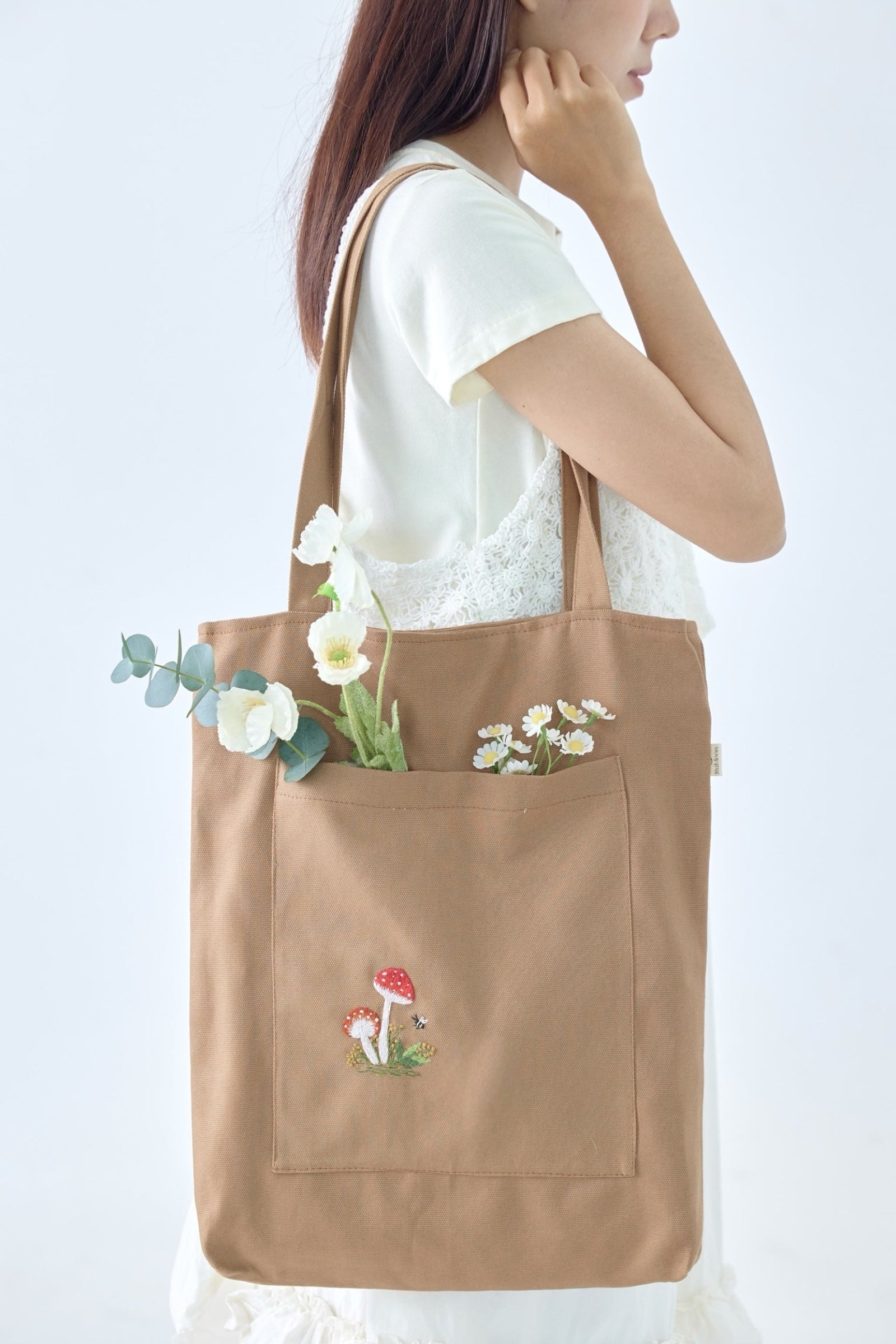 Mushroom Front Pocket Embroidery Tote Bag Brown worn on shoulder, featuring a large front pocket with red mushroom embroidery and floral accents.