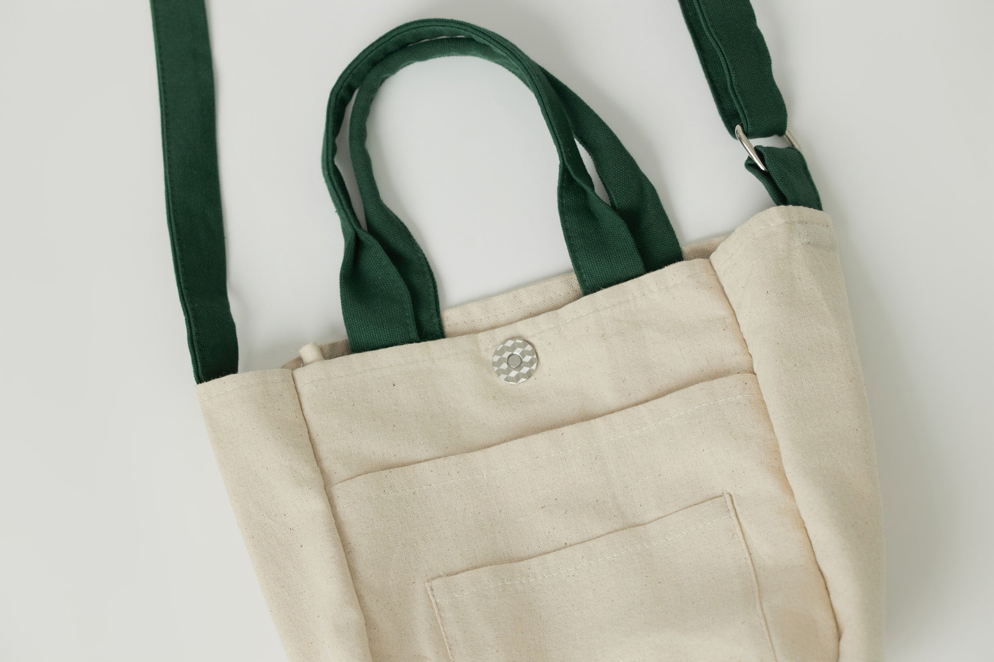 Close-up of 2-in-1 green crossbody handbag with floral embroidered handle, showing button closure and inner pocket for functional storage.